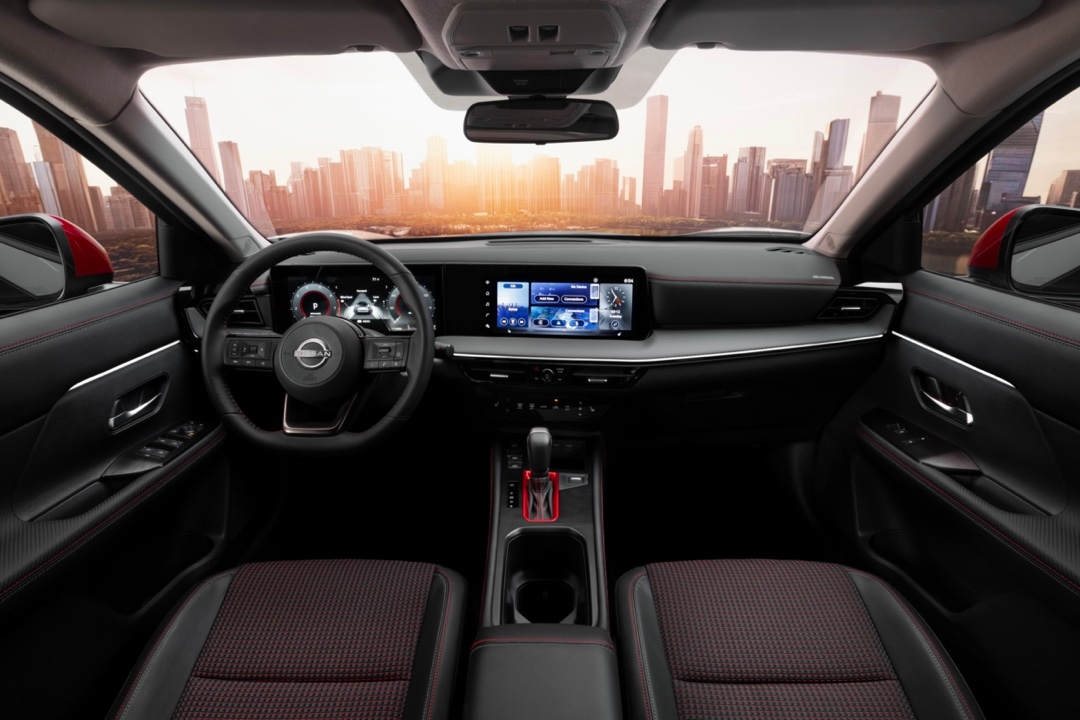 Habitacle du Nissan Kicks 2025 avec sièges sport à surpiqûres rouges et double écran numérique devant un paysage urbain au coucher du soleil.