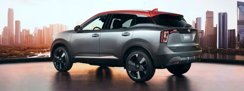 Nissan Kicks 2025 gris et rouge vu de trois quarts arrière avec la ville et les gratte-ciel en arrière-plan.