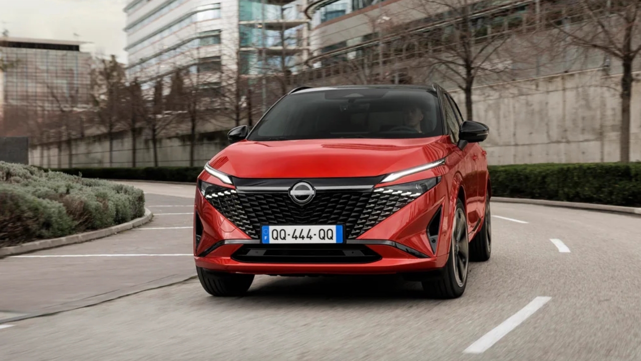 Nissan Qashqai 2025 rouge en mouvement sur une rue bordée d’immeubles modernes.